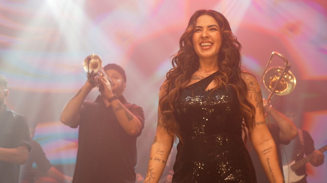 Vocalista da Banda Prime sorrindo com o naipe de metais ao fundo
